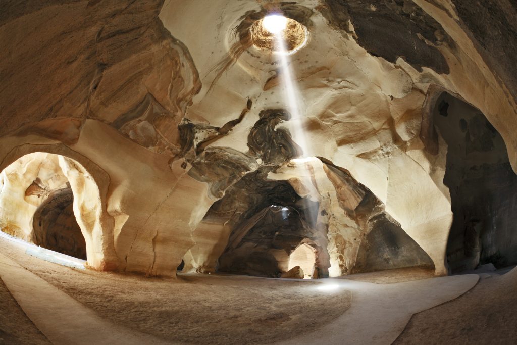 Israel National Park. Bell caves of Beit Guvrin. Picturesque clay arches illuminated by the sun from the hole at the top and side entrances - nesmobile